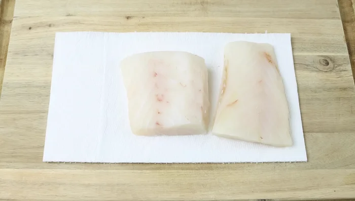 Secar los filetes de bacalao con papel absorbente, sazonarlos y cortarlos en trozos pequeños.
