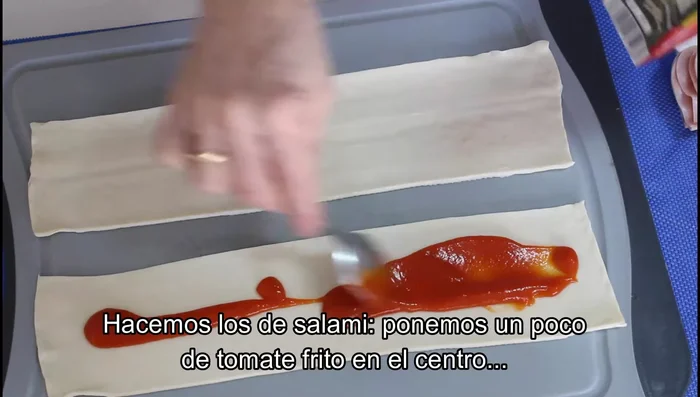 Para los saladitos de salami: Extender un poco de tomate frito en el centro de una tira, colocar lonchas de salami partidas por la mitad, pintar los bordes con huevo batido y enrollar.