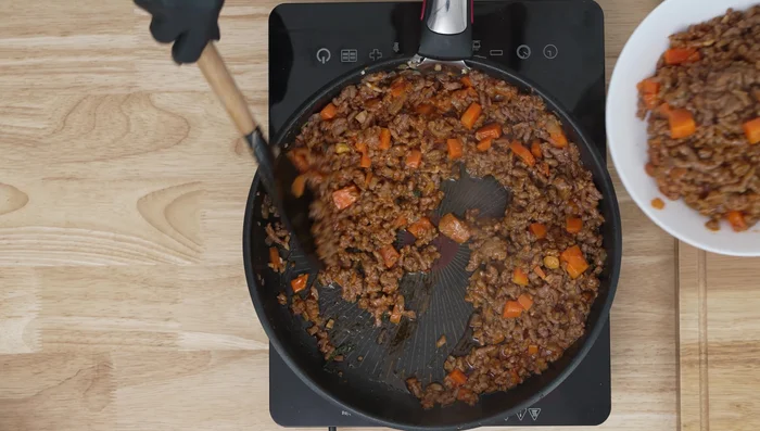 Forma las capas: En el fondo de la sartén, coloca una capa delgada de la salsa de carne como base. Cubre con placas de lasaña crudas partidas para cubrir la superficie sin dejar espacios. Añade una capa generosa de queso.