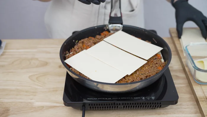 Repite las capas: Repite el proceso: capa de carne, capa de placas de lasaña y queso. La última capa debe ser de carne y una buena cantidad de queso rallado (mozzarella).