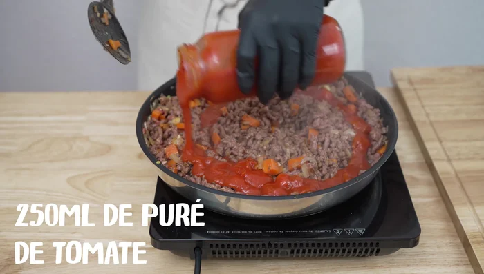 Añade el puré de tomate y albahaca: Agrega 250 ml de puré de tomate y las hojas de albahaca. Si el tomate es ácido, agrega una pizca de azúcar para equilibrar el sabor.