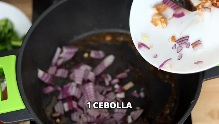 Bajar el fuego al mínimo. Agregar cebolla picada, ajo del aliño, medio pimiento rojo y medio pimiento verde. Cocinar por 5-8 minutos.