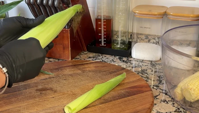 Preparar las hojas de maíz: usar las hojas grandes para envolver y las pequeñas para amarrar (95.2). Superponer hojas pequeñas para formar un cilindro y amarrar en forma de cruz (119.56).