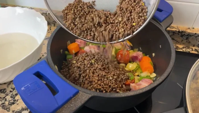 Añadir zanahoria, lentejas, laurel, pimentón, comino, puré de tomate y agua. Remover. Tapar y cocinar a fuego bajo durante 1 hora.