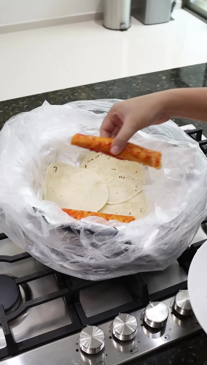 Colocar los taquitos en una olla forrada con papel aluminio y una bolsa de plástico, sobre una capa de tortillas. Agregar un poco de agua a los lados.