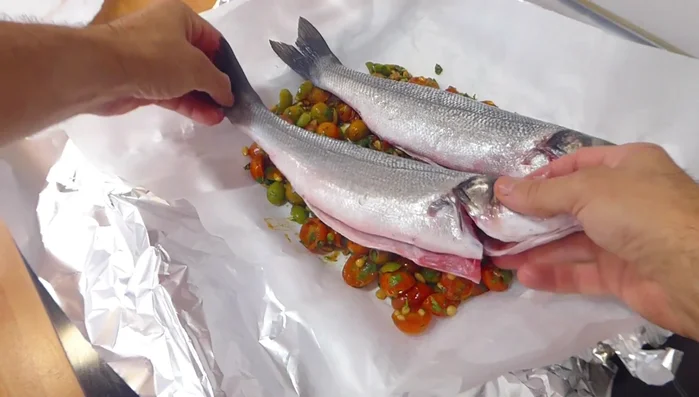 Colocar las lubinas sobre la mezcla y envolverlas bien con el papel de aluminio para cocinar al papillote (160.98).