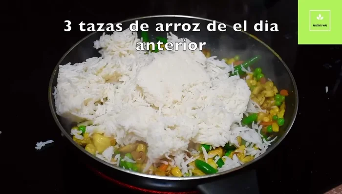 Agregar el arroz cocido del día anterior y mezclar bien con el pollo y las verduras, separando los granos de arroz para que se cocinen uniformemente.