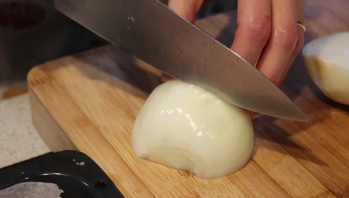 Añadir la cebolla cortada en trozos gruesos y los dientes de ajo partidos por la mitad a la bandeja de horno, junto con las alitas.