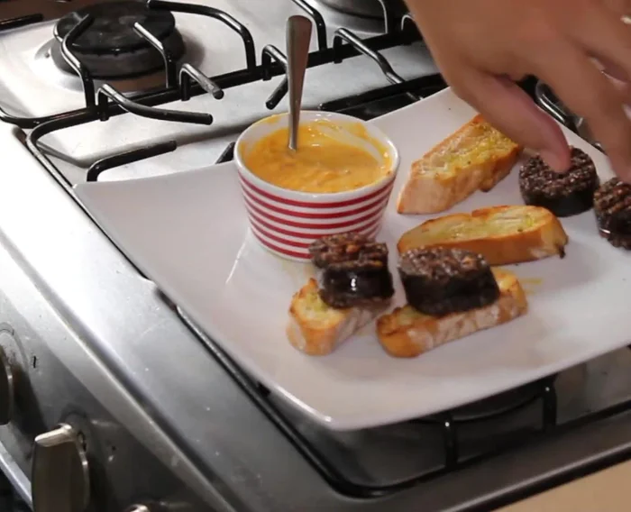 Servir las morcillas sobre pan tostado, con la salsa de pimientos y queso manchego encima (132.48).