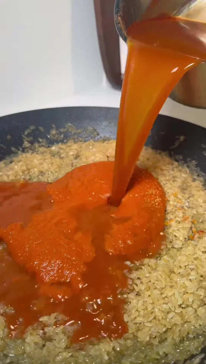 Agregar el arroz a la paella, junto con el sofrito y caldo. Cocinar hasta que el arroz esté casi listo.