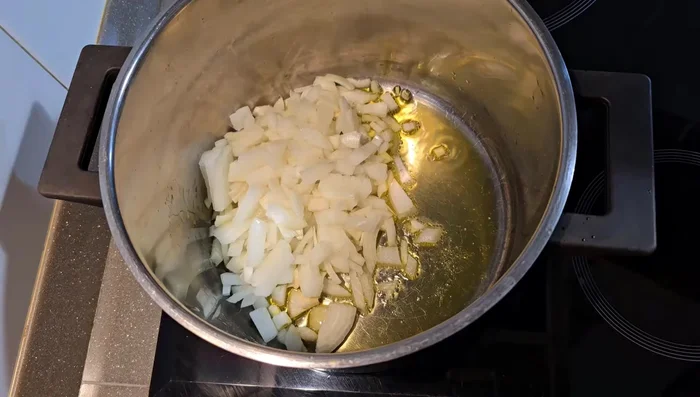 En una olla, añadir el aceite de oliva, la cebolla picada, el puerro y dos zanahorias cortadas. Sofreír a fuego medio.