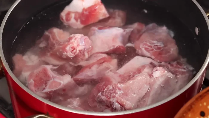Agregar la carne de cerdo, los ajos y la cebolla a una olla con agua. Dejar a cocción a fuego bajo durante aproximadamente 40 minutos, hasta que el agua hierva.