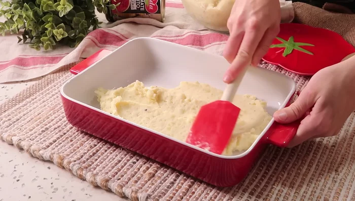 En una fuente para horno (30x20 cm), ponemos una capa fina de puré de patatas, el sofrito de carne y el puré restante. Alisamos y rayamos la superficie con un tenedor.