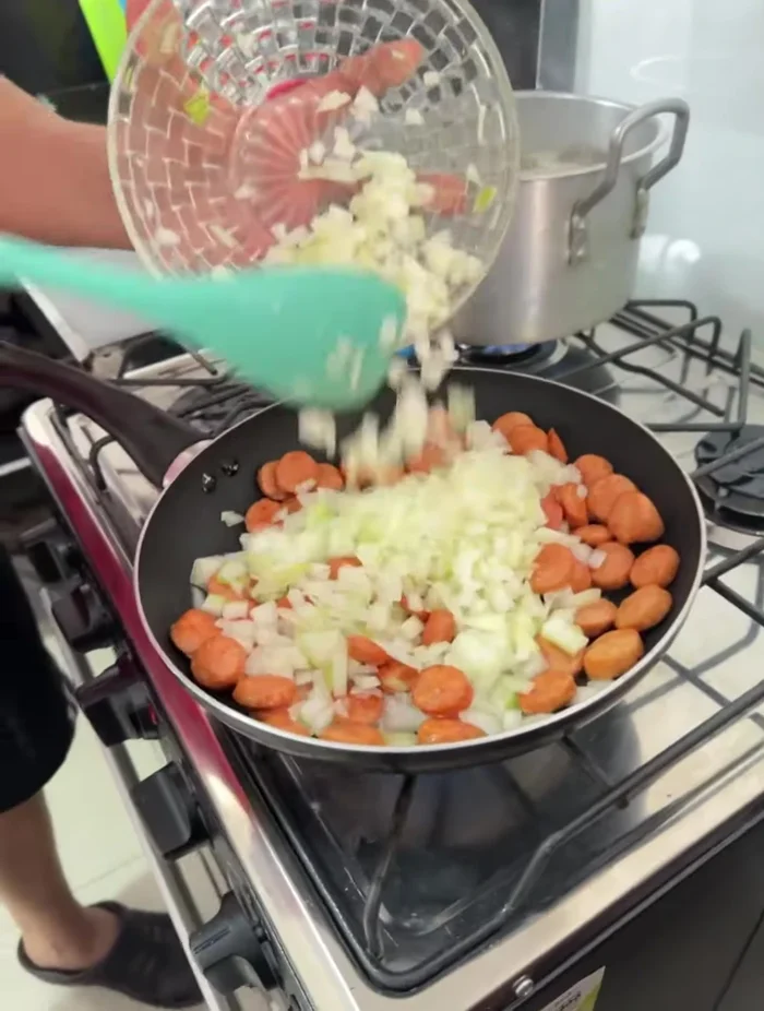 Agregar la cebolla picada a las salchichas sofritas, cocinar hasta que esté bien sofrita. Luego agregar el tomate.