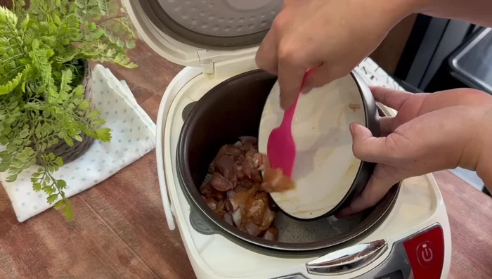 Agregar ingredientes a la olla: Agregar el pollo marinado, la salchicha china (previamente deshuesada y cortada), los hongos chinos (remojados y cortados) y los champiñones a la olla arrocera. Mezclar ligeramente. (129.879)