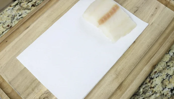 Secar los filetes de bacalao con toallas de papel. Sazonar con sal y pimienta solo por un lado. Cortar en trozos.