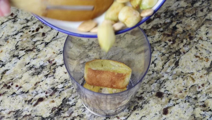 Mientras tanto, transferir el pan frito, las almendras y el ajo a un cilindro de plástico alto. Agregar el perejil picado, sal marina y agua. Licuar hasta obtener un puré fino.