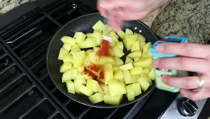 Agregar pimentón español ahumado dulce, comino molido, sal y pimienta a las patatas ligeramente doradas. Mezclar bien.