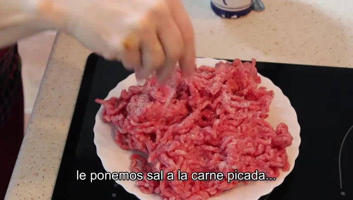A la carne picada, añadir sal, pimienta molida y una pizca de nuez moscada. Mezclar bien y reservar.