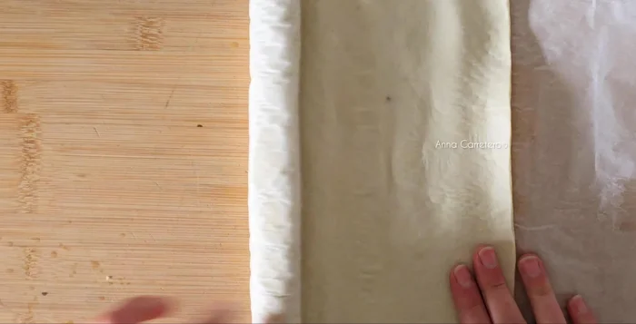 Extiende la plancha de hojaldre y espárcele la crema fría y la canela en polvo. Divide la plancha en ocho partes y enróllalas.
