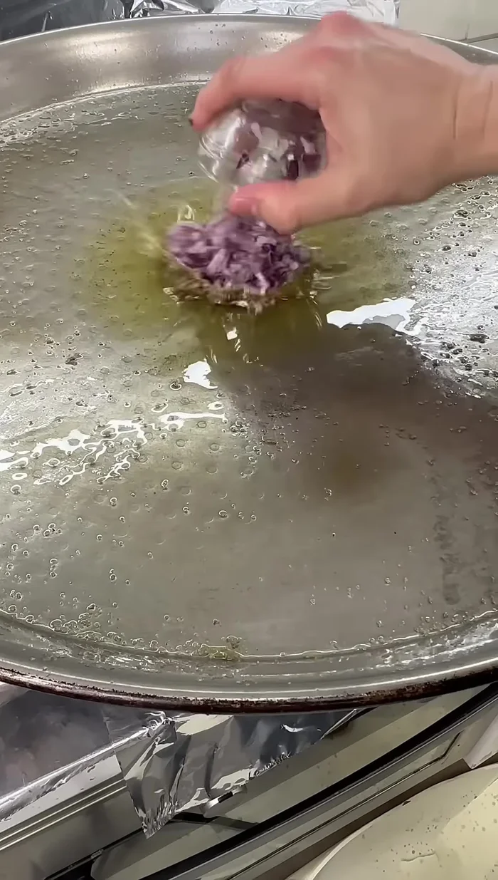 Añadir la cebolla a la paella, cocinarla y reducirla con sal y agua.