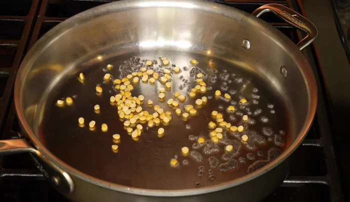 Agrega las semillas de mostaza, chana dal, urad dal, anacardos, chiles rojos secos, hojas de curry, chiles verdes y jengibre. Sofríe hasta que las semillas de mostaza exploten y el chana dal se dore.