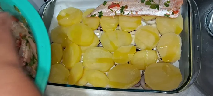 Añade la Meluza: Coloca los filetes de melusa marinada sobre las patatas y cebollas.
