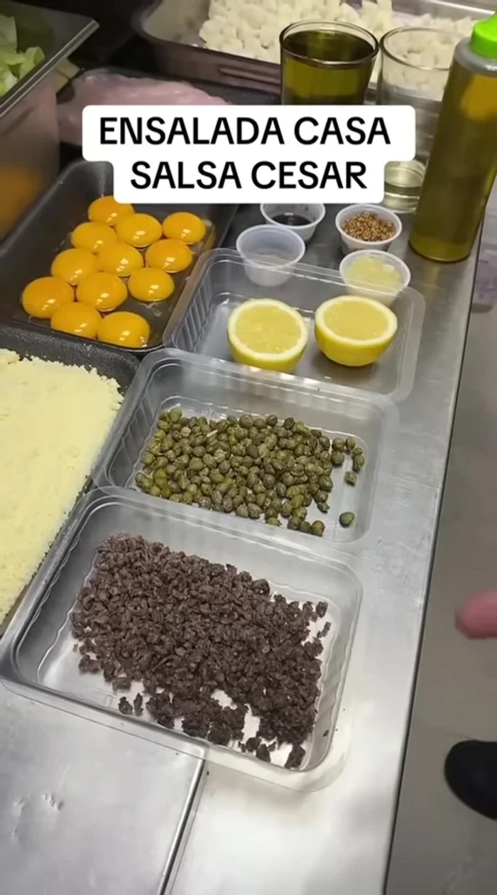 Preparación de la salsa César: Picar finamente las anchoas. Incorporar alcaparras, zumo de limón, yema de huevo, ajo prensado, pimienta en grano, salsa Perrins, mostaza en grano, aceite de oliva suave y el aceite reservado de las anchoas.