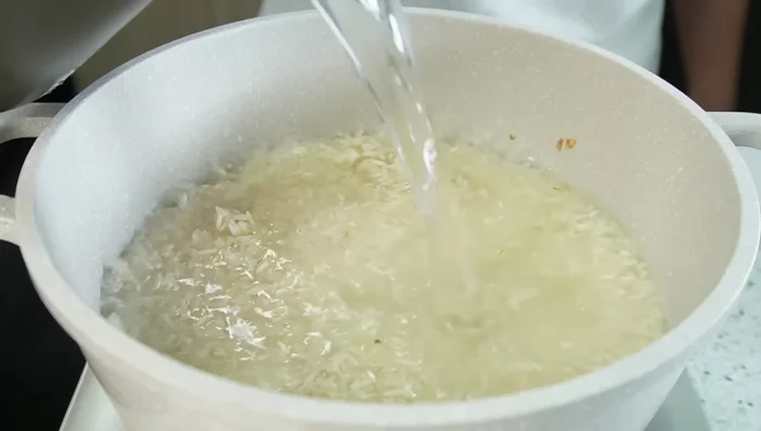 Agregar agua caliente (el doble de la cantidad de arroz), sal y mezclar. Tapar parcialmente y dejar hasta que se formen huequitos. Bajar el fuego, dejar secar completamente, apagar y dejar tapado por 10 minutos.