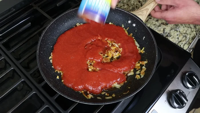 Agregar la salsa de tomate, el caldo, el azafrán, sal, pimienta, y opcionalmente azúcar/bicarbonato/canela y la hoja de laurel. Mezclar bien.