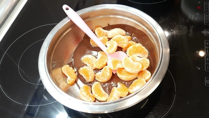 Agregar las mandarinas/naranjas: Una vez fundido el chocolate, añade los gajos de 3 mandarinas (o la cantidad que hayas elegido) y mezcla bien hasta cubrirlas completamente con el chocolate.