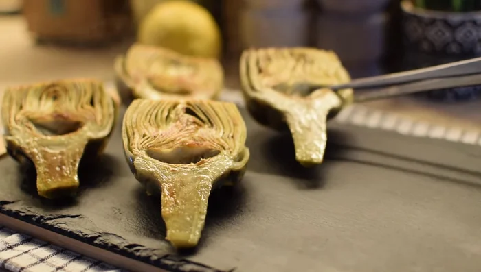 Colocar dos o tres lonchas de jamón ibérico sobre cada alcachofa caliente para que suelte su grasa y sabor.