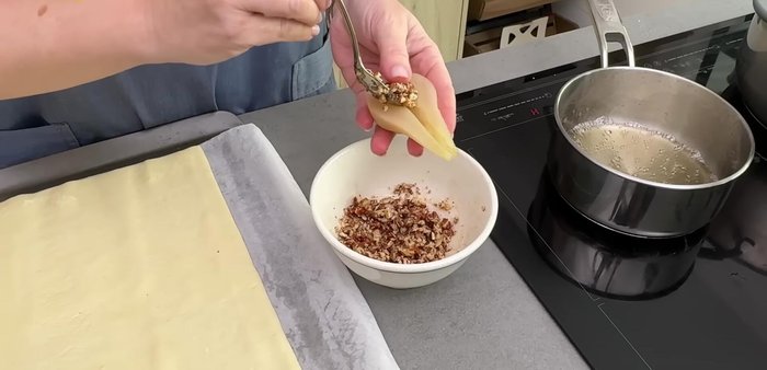 Colocamos la plancha de hojaldre en una bandeja de horno. Rellenamos los huecos de las peras con la mezcla de nueces y miel, y colocamos las mitades de pera sobre el hojaldre (102.28).