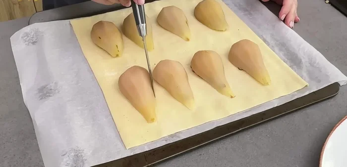 Con una puntilla, marcamos el borde de las peras sin cortar el hojaldre. Cortamos los rabitos por la mitad y los colocamos sobre las peras (decoración opcional) (131.08).