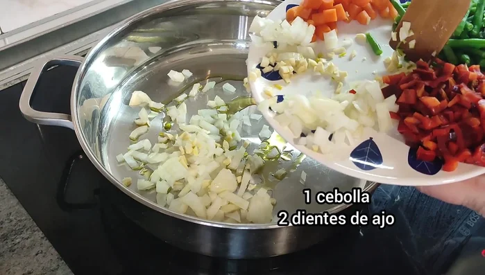 Sofreír la cebolla, el ajo, la zanahoria, los guisantes y las judías verdes en aceite de oliva. Agregar tomate triturado, azafrán, sal y pimienta.