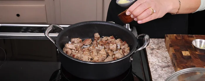 Agregar a la carne de puerco cocida: cebolla picada en cuadritos (sofreír 2 minutos), ajo picado (1 minuto), orégano, comino, y la salsa licuada. Si lo necesita, agregar agua. Dejar cocinar a fuego bajo con la tapa puesta por unos 40 minutos, o una hora en el horno a 350°F (180°C).