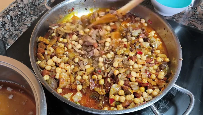 Si se dispone de caldo del cocido, añadirlo hasta cubrir casi por completo la carne y los garbanzos. Dejar cocer a fuego lento hasta que la salsa reduzca y espese. (Si no hay caldo, usar agua).