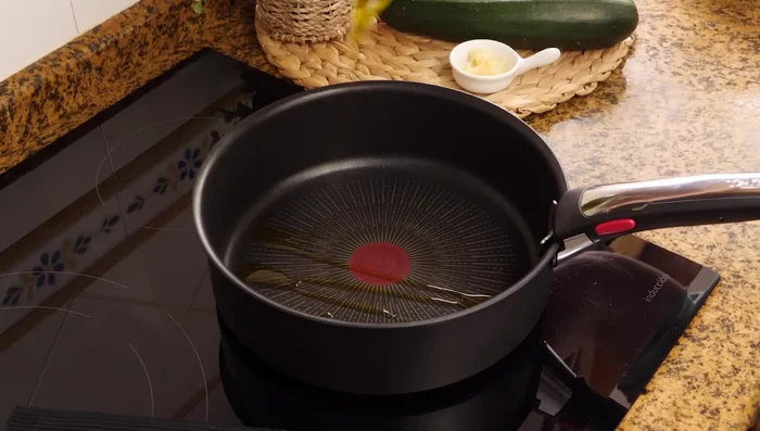 En otra sartén, sofreír el calabacín escurrido con aceite de oliva, 3 dientes de ajo picados y pimienta.