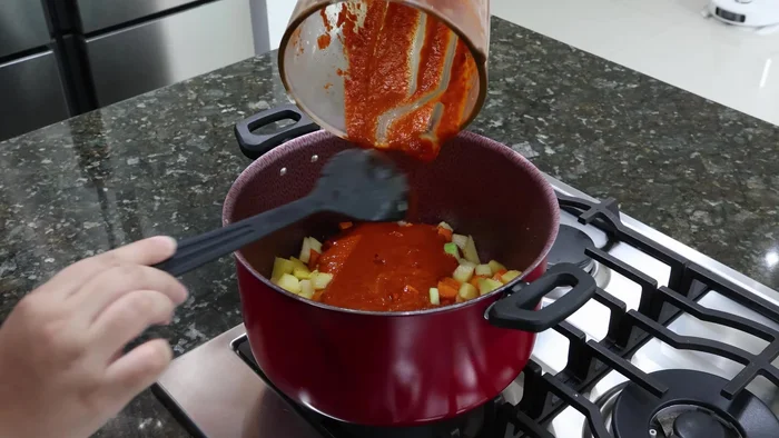 Vierte la salsa licuada sobre las verduras en la olla. Deja guisar antes de agregar 3-4 tazas de agua y más sal al gusto.
