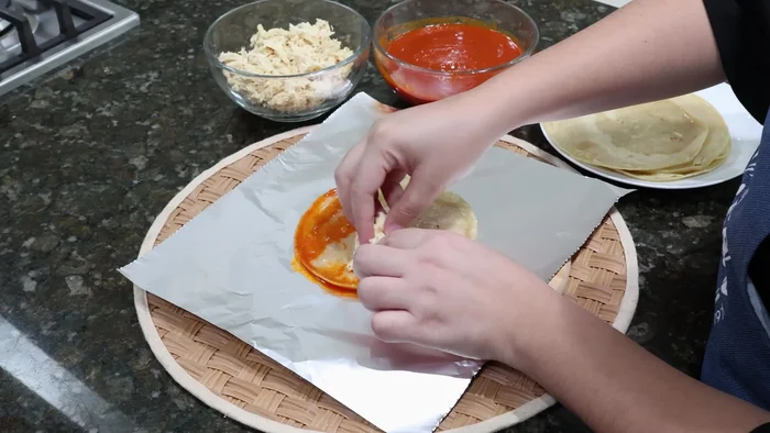 Untar cada tortilla con la salsa roja, rellenar con la pechuga desmenuzada, envolver en papel aluminio como un taquito y sellar bien.