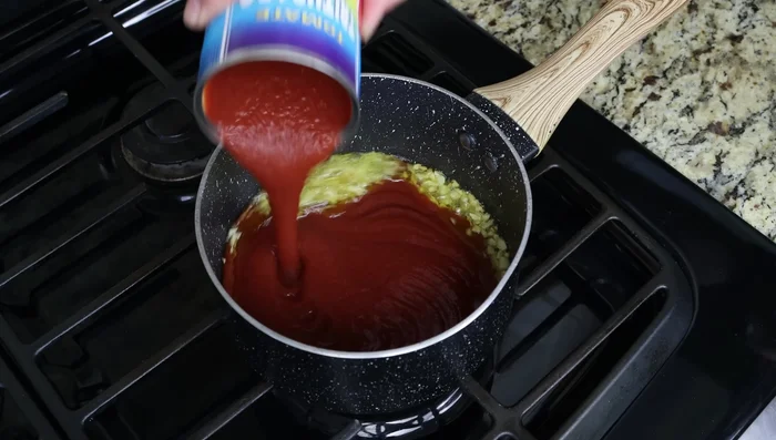 Añadir la salsa de tomate, orégano seco, sal, pimienta y un toque de azúcar. Mezclar bien y dejar hervir a fuego lento para que se desarrollen los sabores.