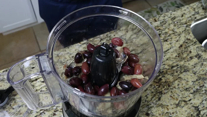 Agregar las aceitunas Kalamata, alcaparras, ajo, orégano, tomillo, jugo de limón, sal y pimienta al procesador de alimentos.