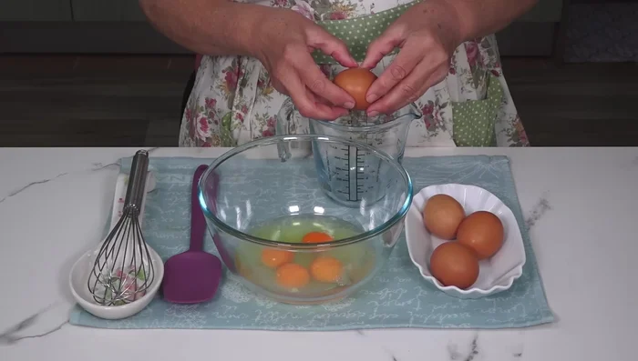 Preparamos la mezcla del flan: En un recipiente, batimos los huevos enteros, las yemas, la esencia de vainilla y el azúcar hasta que se disuelva. Añadimos la leche y mezclamos bien. Pasamos la mezcla por un colador para eliminar posibles grumos o espuma.