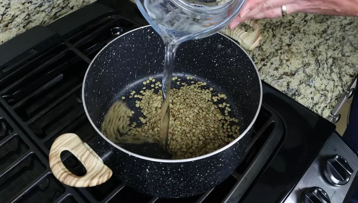 Añadir las lentejas a una olla con agua y una hoja de laurel. Llevar a ebullición a fuego alto, luego bajar el fuego a mínimo y cocinar a fuego lento durante 15-20 minutos o hasta que estén tiernas.