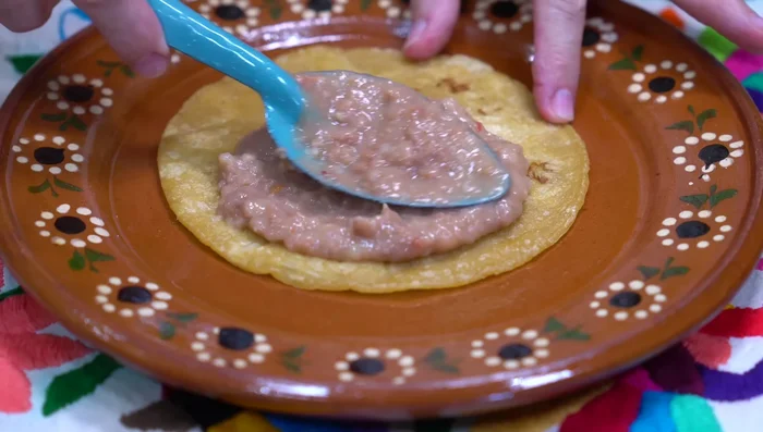 En una tortilla de maíz frita, colocar una capa de frijoles refritos, una rebanada de jamón, el huevo estrellado y la salsa de chiles.