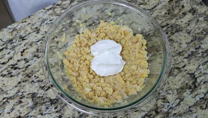 Añadir el yogur griego, la mostaza de Dijon, el pepino inglés picado, la cebolla roja picada, los pepinillos picados, el ajo rallado, el cebollino picado, el zumo de limón, sal y pimienta al puré de garbanzos.