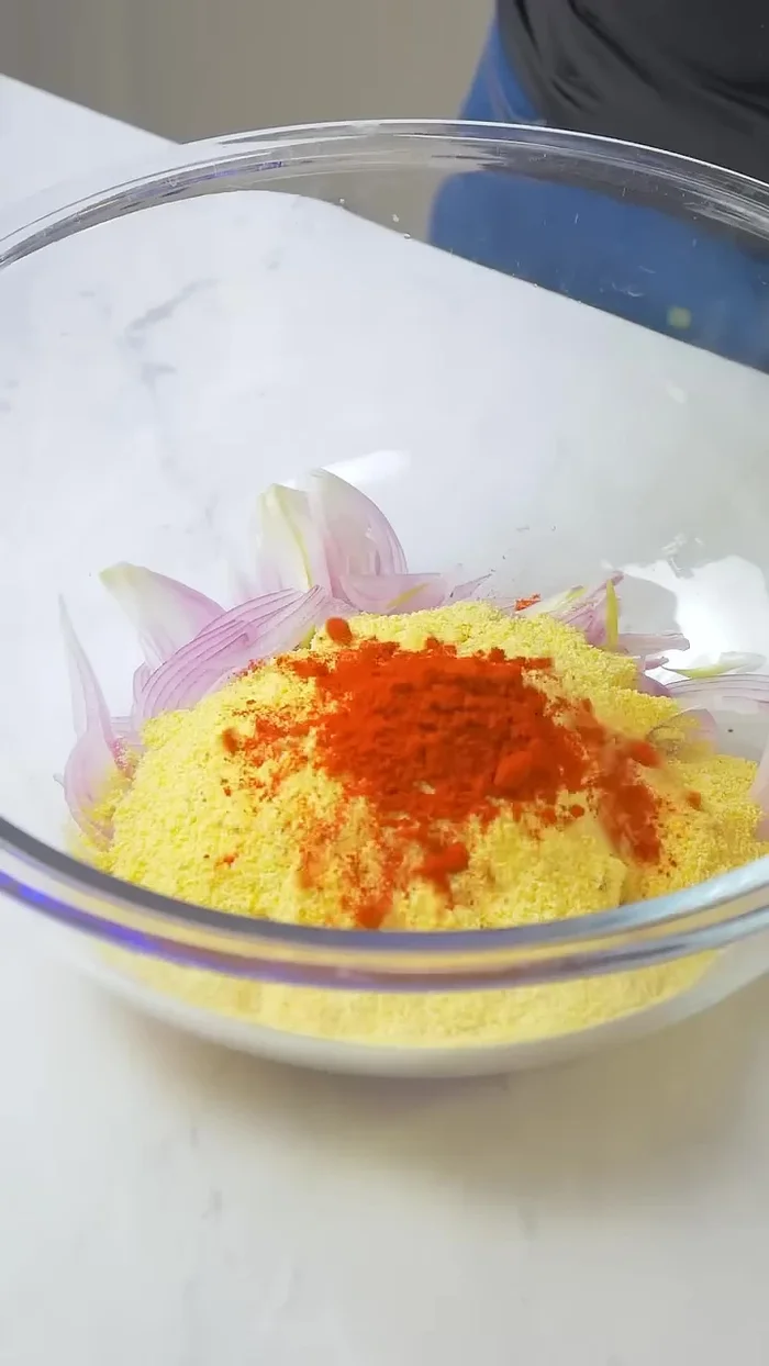En un bowl grande, mezcla las cebollas con una taza de harina de garbanzo, una cucharadita de pimentón en polvo, otra de ajo en polvo, pimienta negra y sal al gusto. Si la masa está seca, añade unas gotitas de agua.
