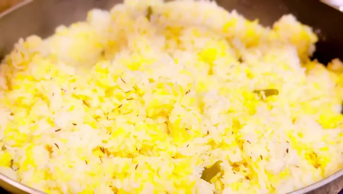 Armar el biryani: Separar el arroz cocido para hacer capas en la olla. Agregar la carne cocida, la cebolla frita caramelizada y la mezcla de leche. Agregar ghee clarificado y el arroz cocido en capas, repitiendo el proceso.