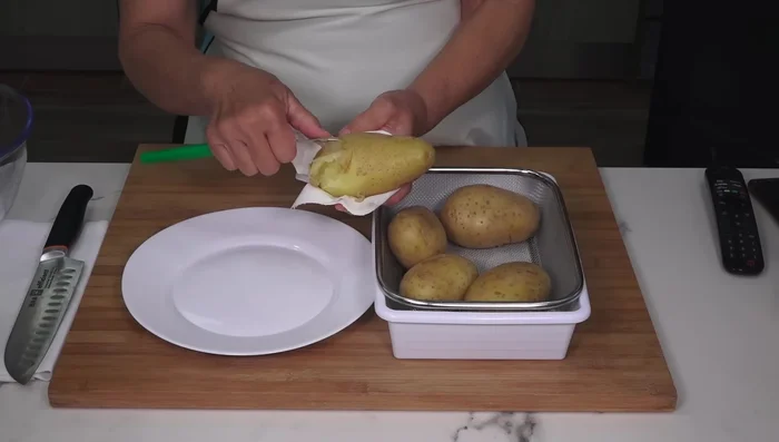 Pelar las patatas aún calientes con ayuda de una servilleta y cortarlas en trozos pequeños.