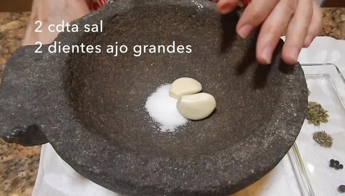 En un molcajete (o licuadora), moler la sal y el ajo hasta obtener una pasta fina. Agregar las especias (comino, orégano, tomillo, pimienta negra, pimienta gorda) y moler hasta integrar.